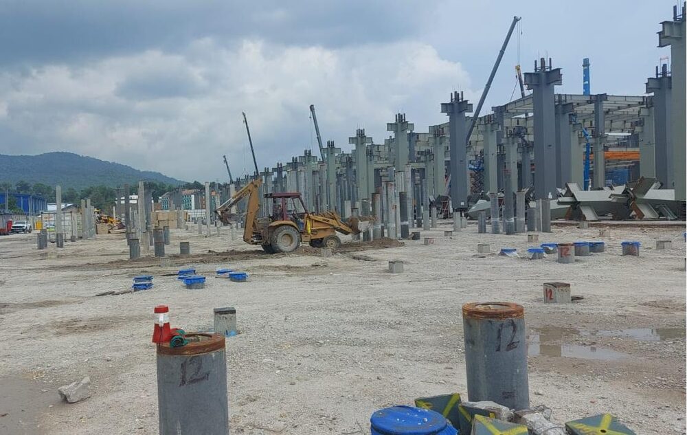 Piling rig and crane driving concrete piles at an industrial site